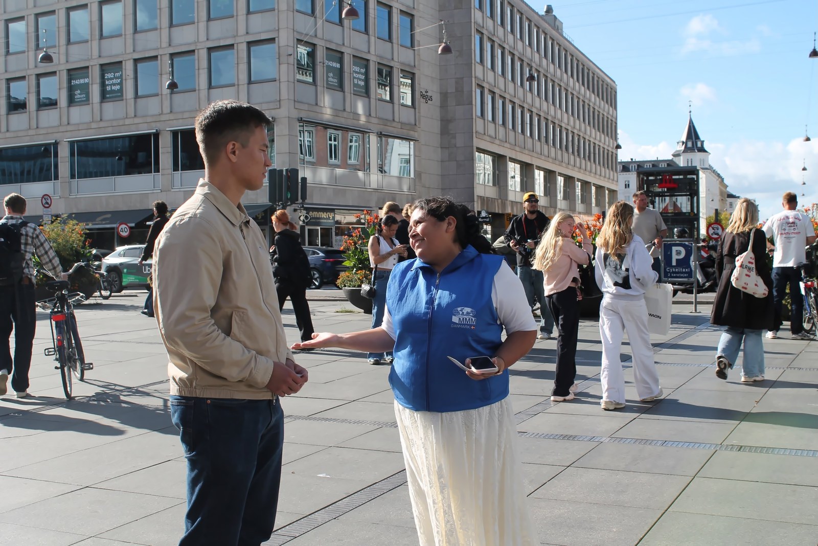 Una hermana con chaleco azul conversa con un joven en una plaza