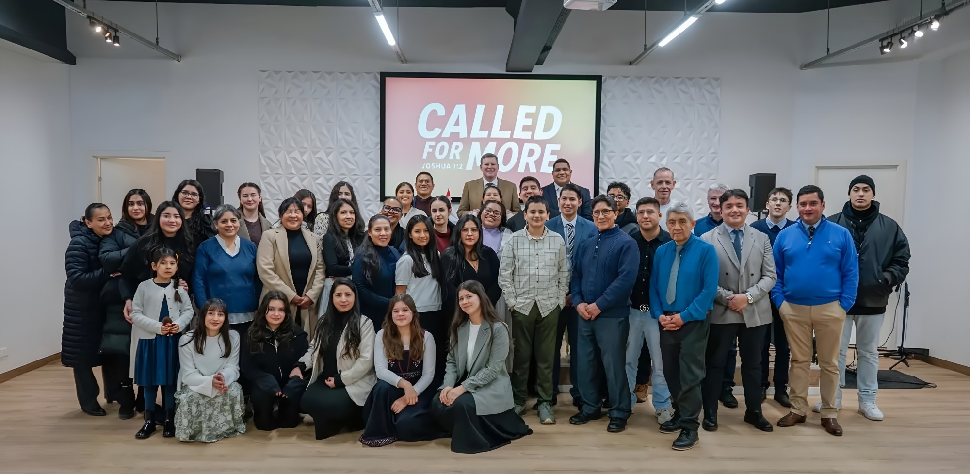 La congregación de MMM Danmark reunida en su local, bajo una pantalla que dice «Called for more»